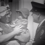 Curly in drag, holding the baby, talking with police officer Bud Jamison