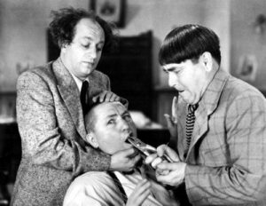 Photographic still of the Three Stooges (Moe Howard, Larry Fine, Curly Howard) preparing to pull one of Curly's teeth with a pliers from the Three Stooges short film I Can Hardly Wait (1943).