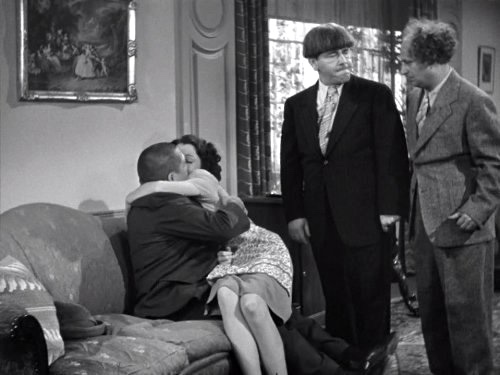 Curly helps make the wife's husband jealous, while Moe and Curly watch, in "Babess in Arms"